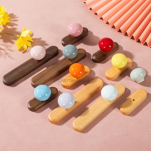 Puede incluir: Una colección de tiradores de cajón decorativos de madera con pomos esféricos de colores. Los tiradores son de varios colores, incluyendo rosa, azul, naranja y amarillo. Algunos tiradores son de color marrón oscuro, otros de madera clara.