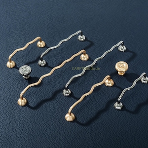 Puede incluir: Una taza de cerámica blanca con un asa negra y el texto "But First, Coffee" en un estilo manuscrito. La taza está sobre una superficie blanca. La taza mide 10 cm de alto.