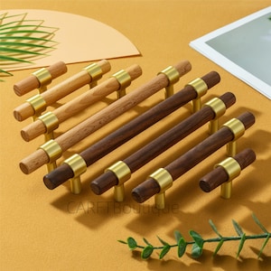 Peut inclure: Ensemble de poignées de meubles en bois de différentes nuances de brun, avec des accents métalliques dorés. Les poignées sont disposées en diagonale sur une surface jaune moutarde. Le texte "CARETBoutique" est visible.