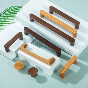 May include: A collection of wooden cabinet hardware, including various sizes of handles and knobs. The handles are in shades of brown and tan, with a curved design. The knobs are round and also made of wood.