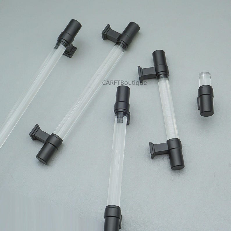 K&ouml;nnte beinhalten: Mehrere transparente Acrylr&ouml;hren mit schwarzen Beschl&auml;gen sind auf einer hellgrauen Oberfl&auml;che angeordnet. Die R&ouml;hren haben eine zylindrische Form und sind mit schwarzen rechteckigen Halterungen verbunden. Eine kleinere R&ouml;hre mit schwarzen Beschl&auml;gen ist ebenfalls vorhanden. Der Text "CARFTBoutique" ist sichtbar.