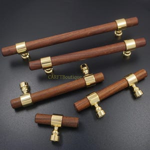 Peut inclure: Ensemble de poignées de meubles en bois avec des détails en métal doré. Les poignées ont une barre cylindrique en bois et sont fixées à la base par un anneau en métal doré. Idéales pour les armoires, les tiroirs ou les meubles.