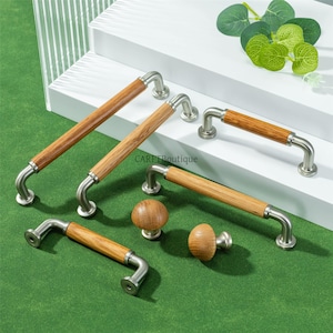 May include: A collection of cabinet hardware, including several wooden and metal handles and two wooden knobs. The handles have a light brown wooden center and curved metal ends. The knobs are round and made of the same light brown wood.