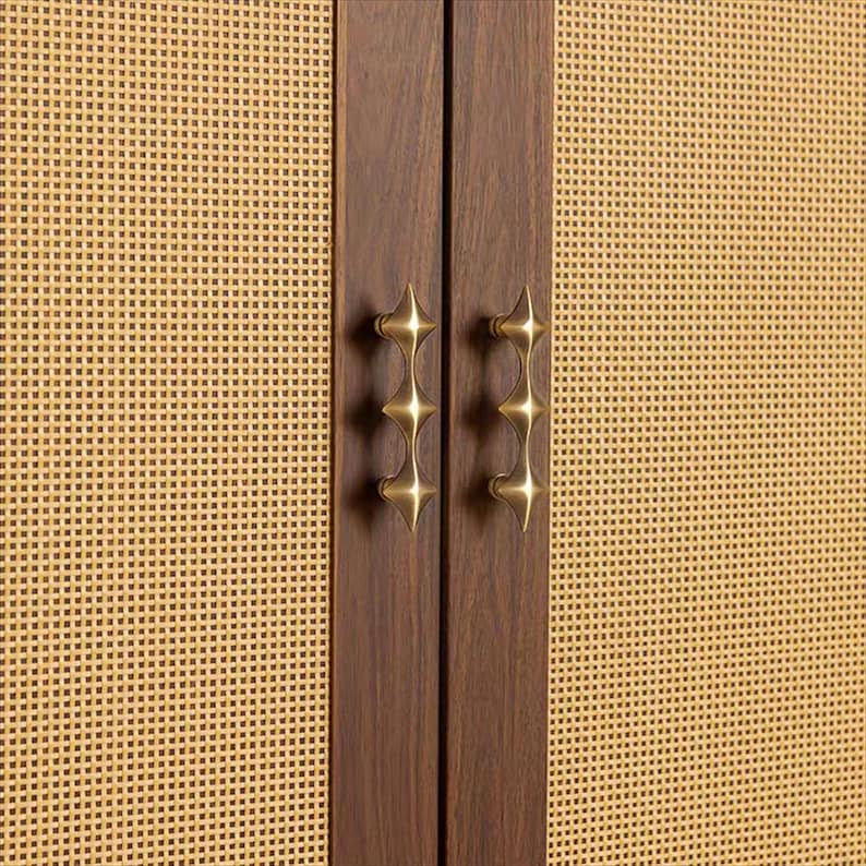 以下が含まれることがあります： 織り込まれた明るい黄色の前面と濃い茶色の木製のドアを備えたキャビネットのクローズアップ。ドアには真鍮色の星型のハンドルが付いています。キャビネットのデザインは、ミッドセンチュリーモダンな美学を示唆しています。