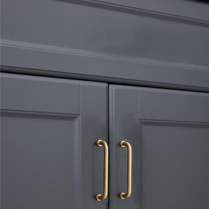 May include: Close-up of a section of a grey cabinet with two gold-coloured, curved bar handles. The cabinet doors are painted a solid grey colour, and the handles are mounted vertically.