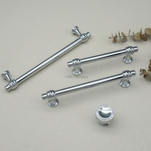 May include: A collection of polished silver cabinet hardware, including a long bar handle, two shorter bar handles, and a round knob. The hardware has a decorative design and is displayed on a neutral background.