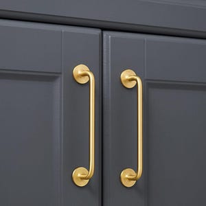 May include: Close-up of two cabinet doors painted a dark gray. Each door has a gold-colored, curved handle. The handles are mounted with circular plates at the top and bottom, creating a sleek, modern look.
