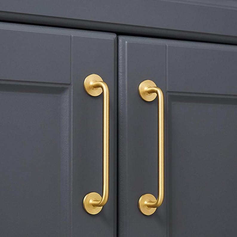 May include: Close-up of two cabinet doors painted a dark gray. Each door has a gold-colored, curved handle. The handles are mounted with circular plates at the top and bottom, creating a sleek, modern look.