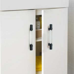 K&ouml;nnte beinhalten: Wei&szlig;e Schrankt&uuml;ren mit schwarzen und transparenten Acryl-Stangengriffen. Die Schrankt&uuml;ren sind leicht ge&ouml;ffnet und geben einen Blick ins Innere frei. Die Griffe sind zylindrisch und vertikal montiert.