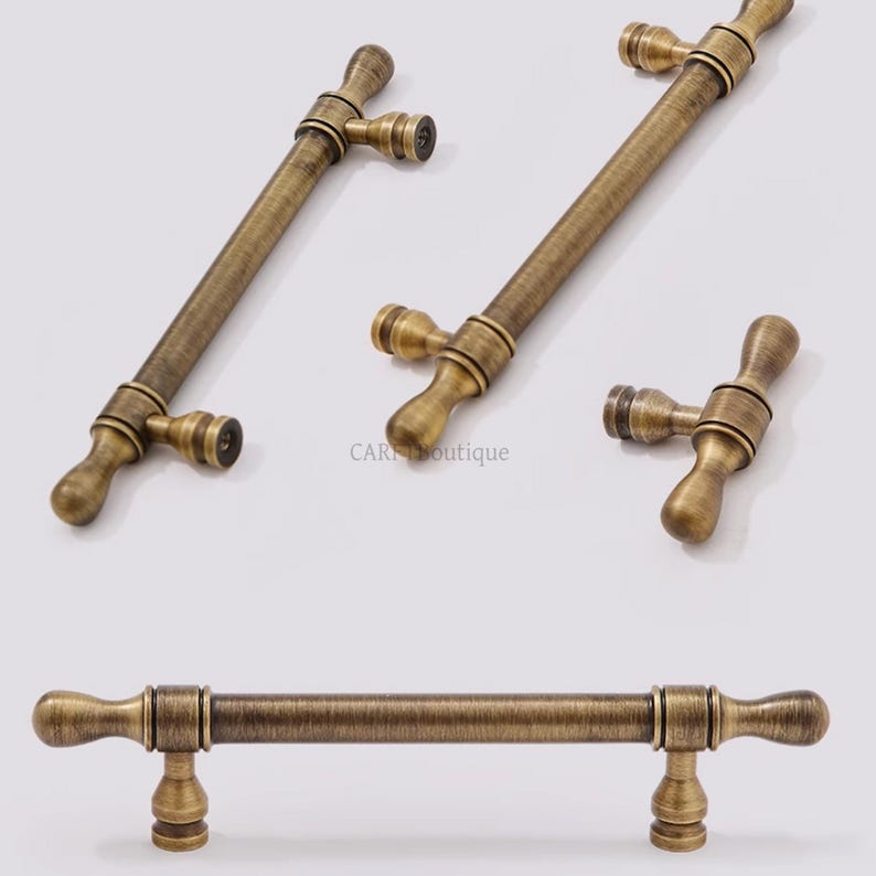 K&ouml;nnte beinhalten: Antike Messing-Schrankgriffe und -kn&ouml;pfe. Die Hardware hat ein T-f&ouml;rmiges Design mit einer zylindrischen Stange und dekorativen Enden. Die Griffe haben ein Vintage-Aussehen mit einer warmen, goldbraunen Farbe. Mehrere St&uuml;cke sind abgebildet.
