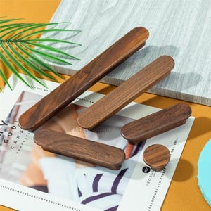 May include: A selection of wooden cabinet pulls and a knob in different sizes. The pulls are rectangular with rounded ends, and the knob is circular. The wood grain is visible. The items are arranged on a magazine with text.