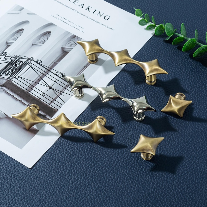 以下が含まれることがあります： 真鍮とシルバー仕上げの装飾キャビネットハードウェア。 ハードウェアには、星型のプルとノブが含まれています。 プルは複数の星のポイントで湾曲しています。 ノブは単一の星の形をしています。 ハードウェアは濃い青色の表面に表示されます。