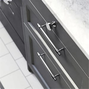 Peut inclure: Gros plan sur une armoire grise &agrave; deux tiroirs, avec des poign&eacute;es de barre chrom&eacute;es polies et un bouton rond. L'armoire est pos&eacute;e contre un comptoir en marbre blanc. Les poign&eacute;es mesurent environ 20 cm de long.