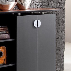 May include: A dark grey cabinet with two doors and white, fan-shaped handles. The cabinet has a wooden top with decorative bowls. Books and a vintage camera are visible on the shelves.