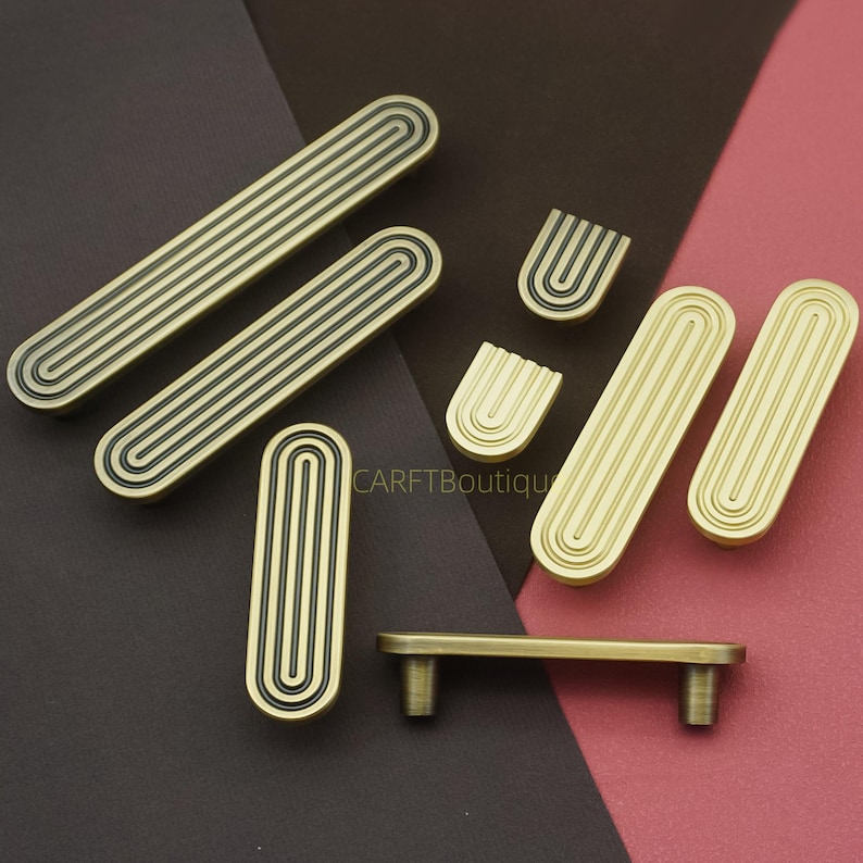 Puede incluir: Un conjunto de herrajes de gabinete de lat&oacute;n antiguo, que incluye manijas y perillas. El hardware presenta un dise&ntilde;o acanalado con detalles en negro. La imagen incluye el texto "CARFTBoutique".