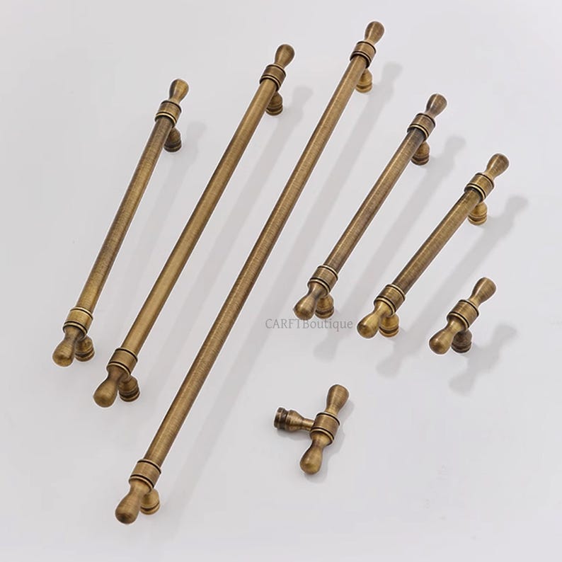 K&ouml;nnte beinhalten: Eine Sammlung antiker Messing-Schrankgriffe und -kn&ouml;pfe in verschiedenen Gr&ouml;&szlig;en. Die Hardware hat ein klassisches Design mit einem warmen, gealterten Finish. Die Griffe reichen von kleinen Kn&ouml;pfen bis zu langen Stangengriffen, ideal f&uuml;r M&ouml;bel.