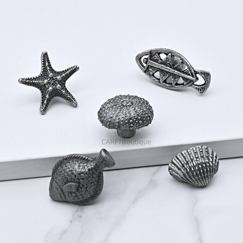 Peut inclure: Ensemble de cinq boutons de meuble argent&eacute;s sur le th&egrave;me marin. Les boutons comprennent une &eacute;toile de mer, un poisson, un oursin, un motif en forme de poisson et un coquillage. Les boutons sont en m&eacute;tal et ont une surface textur&eacute;e et d&eacute;taill&eacute;e.