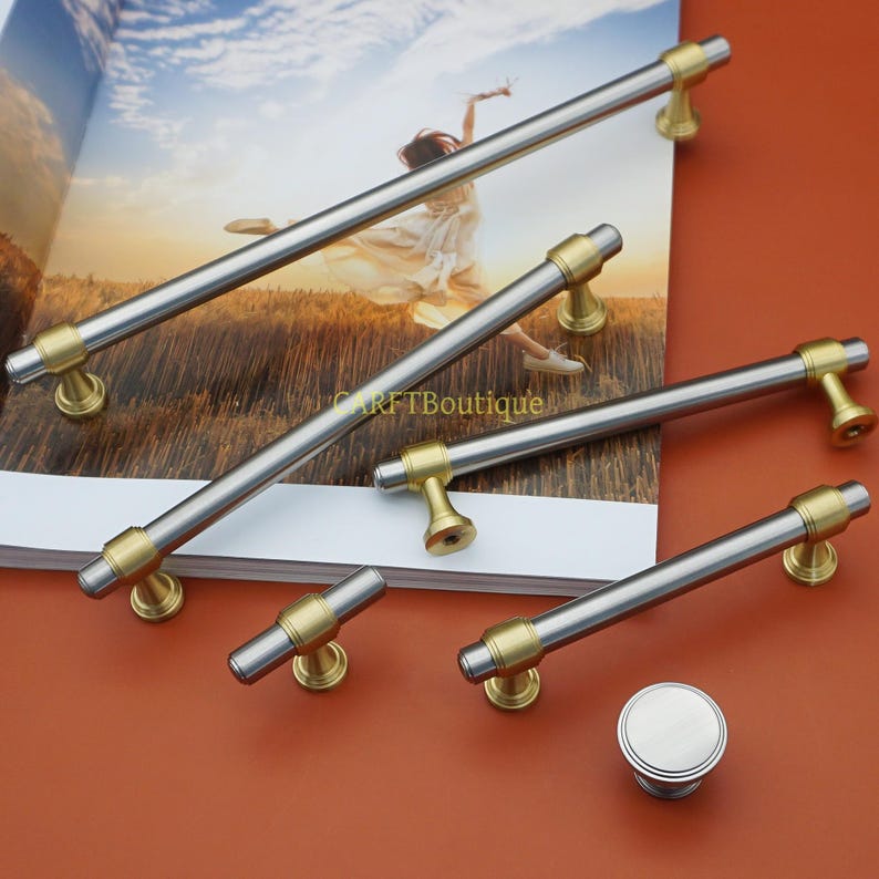 Pode incluir: Uma cole&ccedil;&atilde;o de ferragens para arm&aacute;rios, incluindo v&aacute;rias puxadores de barra prateados e dourados e um bot&atilde;o redondo. Os puxadores t&ecirc;m um acabamento prateado escovado com detalhes dourados. O hardware &eacute; exibido em uma revista.