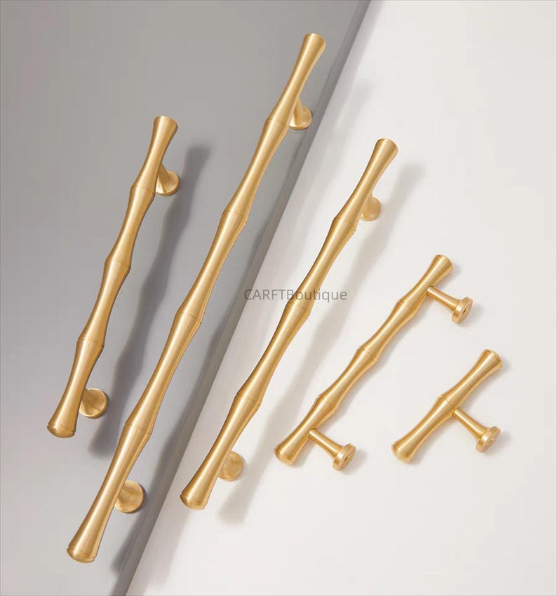 K&ouml;nnte beinhalten: Eine Sammlung goldfarbener T&uuml;rgriffe mit Bambus-Design. Die Griffe variieren in Gr&ouml;&szlig;e und Form und haben eine glatte, metallische Oberfl&auml;che. Das Bild ist vor einem neutralen grau-wei&szlig;en Hintergrund platziert.