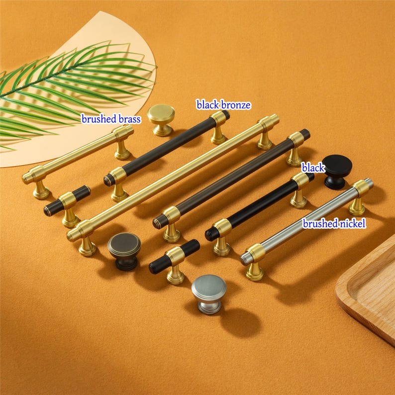 Pode incluir: Uma cole&ccedil;&atilde;o de puxadores e puxadores de arm&aacute;rio em v&aacute;rios acabamentos. Os acabamentos incluem lat&atilde;o escovado, bronze preto, preto e n&iacute;quel escovado. Apresentado em uma superf&iacute;cie laranja-marrom.