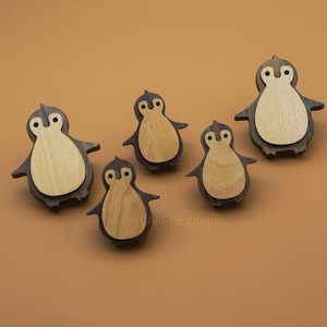 May include: A collection of six wooden penguin figurines. Each penguin has a dark brown body and light brown belly. The penguins are arranged on a solid brown background. The figurines vary slightly in size.