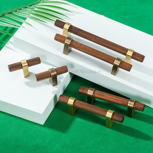 May include: A collection of wooden cabinet pulls with brass-colored hardware. The pulls have a dark brown, cylindrical handle and are mounted on a brass-toned base. The hardware is arranged on a white surface against a green background.