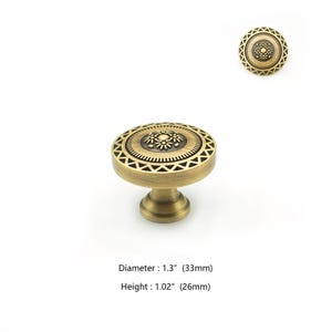May include: A bronze-colored cabinet knob with a decorative floral and geometric design. The knob has a diameter of 1.3 inches and a height of 1.02 inches. The design includes a central floral pattern surrounded by a circular geometric border.
