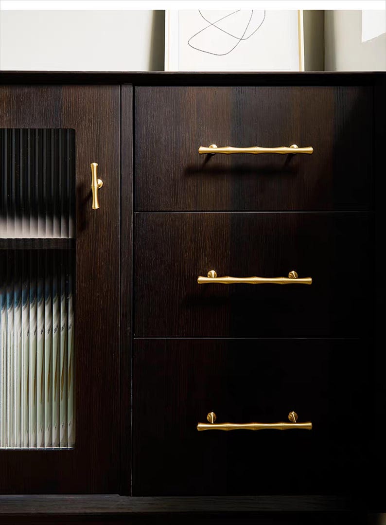 K&ouml;nnte beinhalten: Dunkler Holzschrank mit drei Schubladen und einer Glast&uuml;r. Der Schrank hat goldfarbene, astf&ouml;rmige Schubladengriffe und einen passenden Griff an der T&uuml;r. Das Holz hat eine satte, dunkelbraune Oberfl&auml;che.