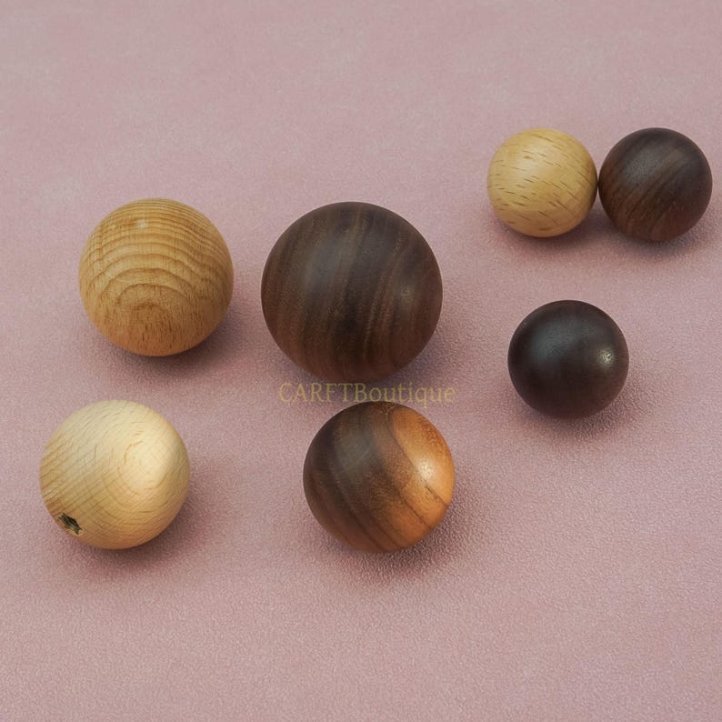 May include: A collection of wooden spheres in various shades of brown and tan. The spheres vary in size and wood grain patterns. Some spheres are light-colored, while others are dark, creating a contrast. The spheres are arranged on a pink surface.