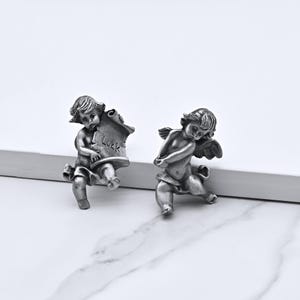 Peut inclure: Deux figurines de ch&eacute;rubins argent&eacute;s. L'un tient un parchemin avec le mot "Luck". L'autre ch&eacute;rubin a des ailes et est agenouill&eacute;. Les figurines sont d&eacute;taill&eacute;es et ont une esth&eacute;tique vintage.