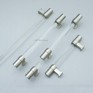 K&ouml;nnte beinhalten: Eine Sammlung von Schrankgriffen aus klarem Acryl und geb&uuml;rstetem Nickel. Die Griffe haben ein zylindrisches Design mit einem klaren Acrylmittelteil und Enden und Befestigungsteilen aus geb&uuml;rstetem Nickel. Das Bild enth&auml;lt den Text "CARFTBoutique".