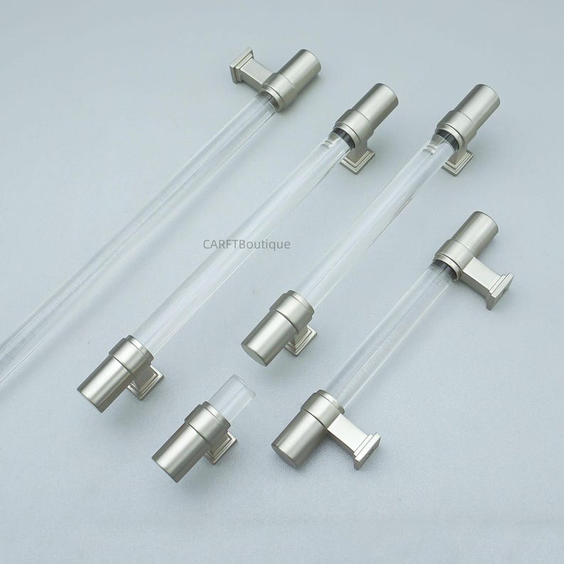K&ouml;nnte beinhalten: Eine Sammlung von Schrankgriffen aus klarem Acryl und geb&uuml;rstetem Nickel. Die Griffe haben ein zylindrisches Design mit einem klaren Acrylmittelteil und Enden und Befestigungsteilen aus geb&uuml;rstetem Nickel. Das Bild enth&auml;lt den Text "CARFTBoutique".