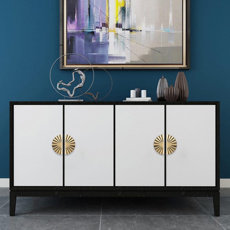 May include: A contemporary white and black cabinet with four doors and gold sunburst handles. The cabinet has a dark wooden frame and is set against a blue wall with artwork.