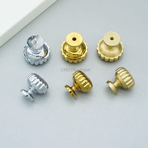 May include: A collection of six decorative cabinet knobs in silver and gold finishes. The knobs have a fluted, rounded design with a scalloped base. The brand name "CARFTBoutique" is visible in the center of the image.