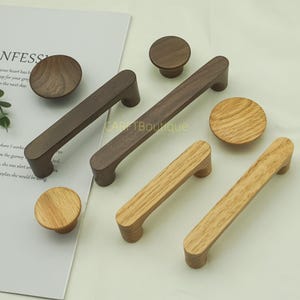Puede incluir: Una colección de tiradores y pomos de madera para armarios. Los pomos son redondos y los tiradores rectangulares con bordes curvos. Los tonos de madera varían desde roble claro hasta nogal oscuro. El texto "CARP Boutique" es visible.
