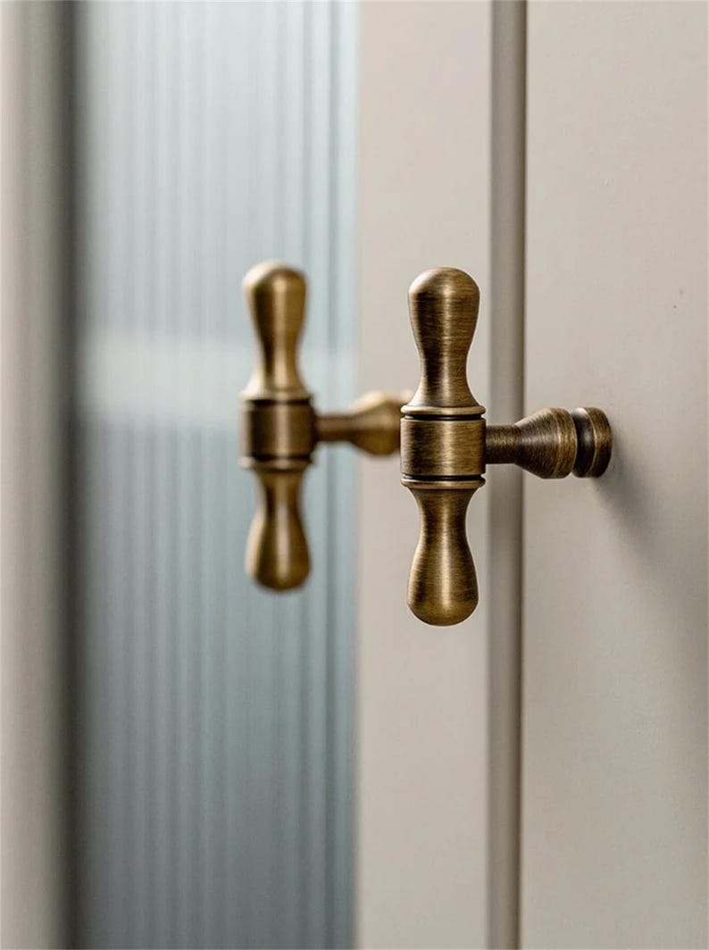 K&ouml;nnte beinhalten: Nahaufnahme von zwei antiken T&uuml;rgriffen aus Messing. Die Griffe haben ein klassisches, elegantes Design mit einem warmen, gealterten Finish. Die Griffe sind an einer hellen T&uuml;r montiert, mit einem unscharfen Hintergrund.