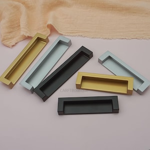 Op de afbeelding: Een assortiment kastgrepen in verschillende kleuren, waaronder goud, zilver en zwart. De grepen zijn rechthoekig met een verzonken handvatontwerp. De afbeelding is genomen vanuit een iets verhoogde hoek, met de verschillende kleuropties.