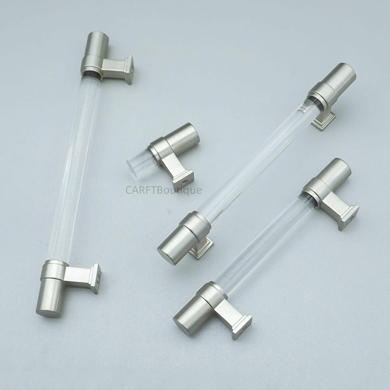 K&ouml;nnte beinhalten: Vier Schrankgriffe mit transparenten Acrylst&auml;ben und Hardware mit geb&uuml;rsteter Nickeloberfl&auml;che. Die Griffe haben ein modernes Design mit zylindrischer Stange und quadratischen Montageplatten. Die Hardware hat eine matte Oberfl&auml;che.