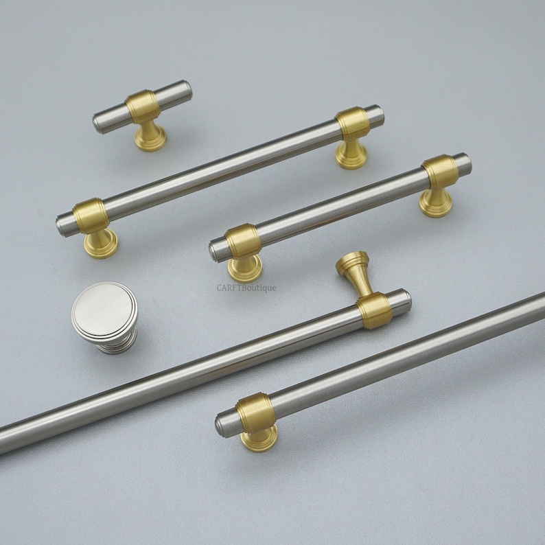 K&ouml;nnte beinhalten: Eine Auswahl an Schrankgriffen und -kn&ouml;pfen in geb&uuml;rsteter Silberausf&uuml;hrung mit goldfarbenen Details. Das Bild zeigt eine Vielzahl von Gr&ouml;&szlig;en und Stilen, darunter ein runder Knopf und Stangengriffe in verschiedenen L&auml;ngen.