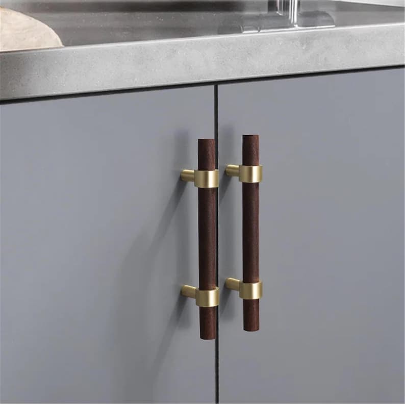 以下が含まれることがあります： 濃い茶色の木製ハンドルと金色の金属アクセントが付いた2つのキャビネットプル。プルは垂直方向に配置され、灰色のキャビネットドアに取り付けられています。デザインはモダンでミニマリストです。