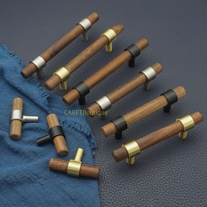 以下が含まれることがあります： シルバー、ゴールド、ブラックの金属アクセントが付いた木製キャビネットプルコレクション。 プルは円筒形の木製ハンドルを備え、家具用に設計されています。 ハードウェアは濃い青色の表面に表示されます。