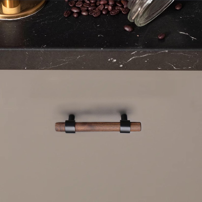 以下が含まれることがあります： 濃い木材のハンドルと黒い金属アクセントが付いたキャビネットプル。ハンドルは円筒形で、豊かで濃い木材で作られているようです。黒い金属製のブラケットは、木材とのモダンなコントラストを提供します。