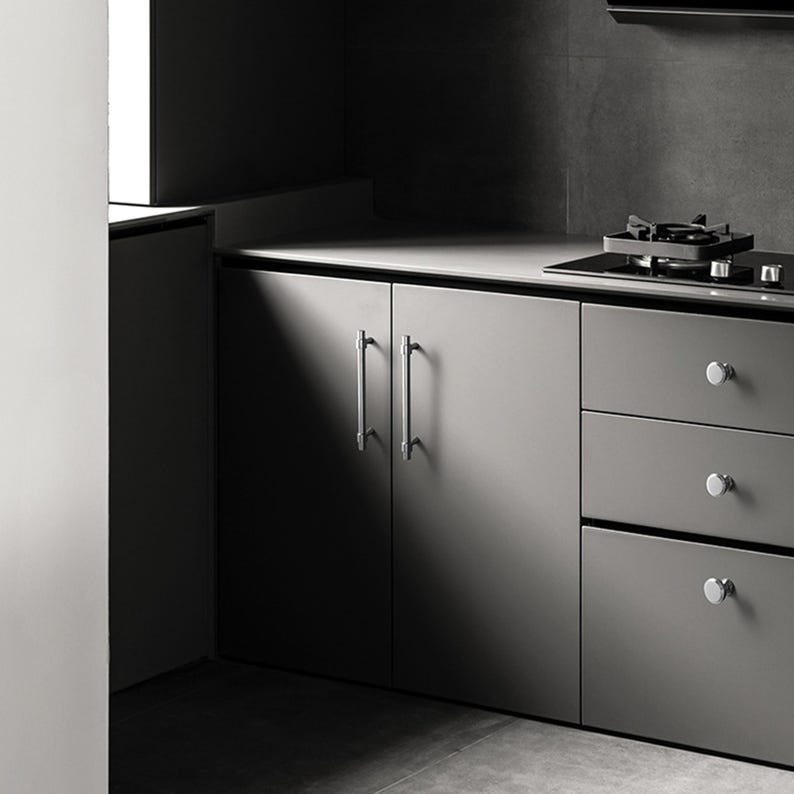 Peut inclure: Une cuisine moderne avec des meubles gris et des poign&eacute;es argent&eacute;es. Le plan de travail int&egrave;gre une table de cuisson &agrave; gaz. La sc&egrave;ne est &eacute;clair&eacute;e par la lumi&egrave;re naturelle, cr&eacute;ant un jeu d'ombres et de lumi&egrave;res.