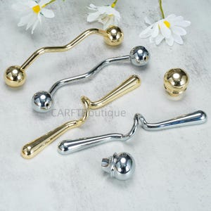 May include: An assortment of decorative cabinet pulls and knobs in gold and silver finishes. The hardware features a curved design with spherical accents. The image includes a variety of shapes and sizes, suitable for furniture or home decor projects.
