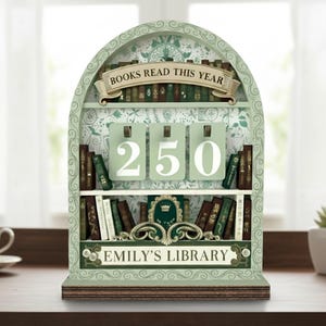 Könnte beinhalten: Ein dekoratives Bücherregal-förmiges Zählwerk mit den Texten "BOOKS READ THIS YEAR" und "EMILY'S LIBRARY". Das Zählwerk zeigt die Zahl "250" auf drei hängenden Karten an. Das Bücherregal ist hellgrün mit floralem Muster und dekorativen Akzenten.