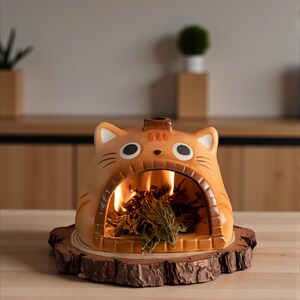 May include: A ceramic cat-shaped incense burner in shades of orange and brown, with a small chimney and a large opening where incense is burning. The burner sits on a round wooden base, creating a cozy, decorative piece.
