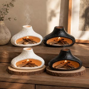 Può includere: Quattro bruciatori di incenso in ceramica a forma di camini in miniatura, due bianchi e due neri, ciascuno con un esterno testurizzato e un'ampia apertura orizzontale. All'interno di ogni bruciatore, piccoli bastoncini di legno bruciano.