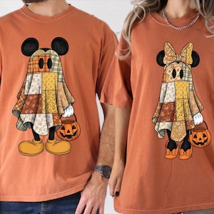 Peut inclure: Deux t-shirts orange brûlé avec des imprimés graphiques de personnages de dessins animés déguisés en fantômes. Un personnage porte un drap en patchwork et tient un seau citrouille, l'autre porte un drap en patchwork avec un nœud et un seau.