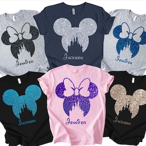 Puede incluir: Varias camisetas con un diseño brillante de Minnie Mouse, que incluye un lazo, una silueta de castillo y nombres personalizados. Las camisetas están disponibles en varios colores como gris, azul marino, negro y rosa.