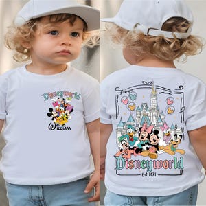Op de afbeelding: Wit T-shirt met Disney-personages, waaronder Mickey Mouse, Donald Duck en Goofy. De voorkant toont "Disneyworld" en de naam "William". De achterkant heeft een kasteelafbeelding en de tekst "Disneyworld Est. 1971".